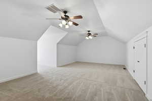 Additional living space above the garage featuring light colored carpet, lofted ceiling, and a ceiling fan