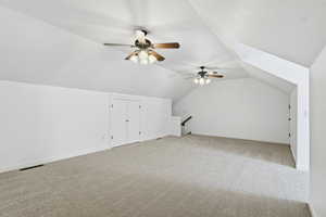 Additional living space above the garage with light colored carpet, vaulted ceiling, and ceiling fan