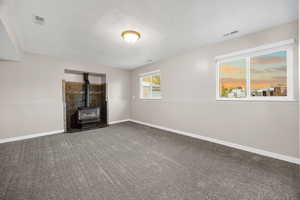 Unfurnished living room featuring a wood stove, carpet flooring, and a textured ceiling