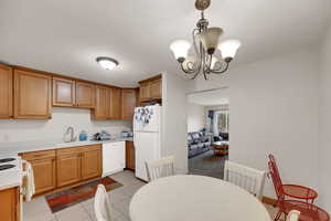 Kitchen featuring light countertops, light tile patterned floors, white appliances, decorative light fixtures, and a chandelier