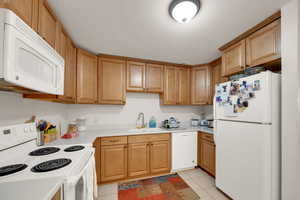 Kitchen with white appliances, light tile patterned floors, light countertops, and light brown cabinetry