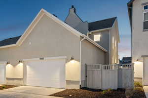 Property exterior at dusk with stucco siding, concrete driveway, an attached garage, and a chimney