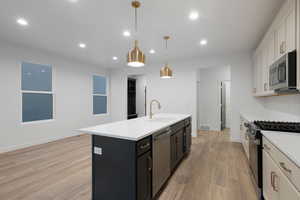 Kitchen featuring white cabinetry, stainless steel appliances, recessed lighting, hanging light fixtures, and a kitchen island with sink