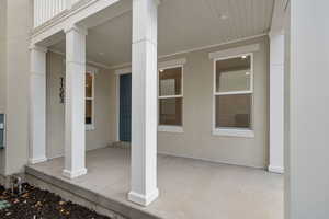 View of exterior entry with covered porch and stucco siding