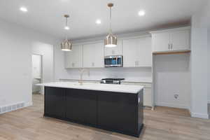 Kitchen featuring pendant lighting, dark cabinets, an island with sink, appliances with stainless steel finishes, and light wood-style floors