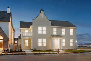 View of front of house featuring a balcony, roof with shingles, a chimney, and stucco siding