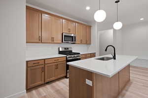 Kitchen featuring stainless steel appliances, decorative light fixtures, backsplash, an island with sink, and light wood-type flooring