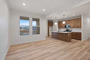 Kitchen with brown cabinetry, recessed lighting, hanging light fixtures, a center island with sink, and light wood-style floors