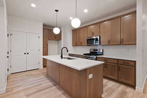 Kitchen with brown cabinetry, appliances with stainless steel finishes, backsplash, a kitchen island with sink, and recessed lighting