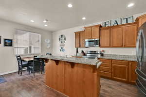 Kitchen with brown cabinets, a breakfast bar area, a kitchen island, recessed lighting, and appliances with stainless steel finishes