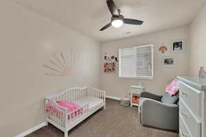 Bedroom featuring a nursery area, carpet, and a ceiling fan