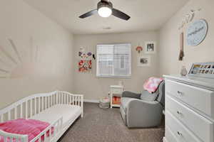 Carpeted bedroom with a crib and ceiling fan