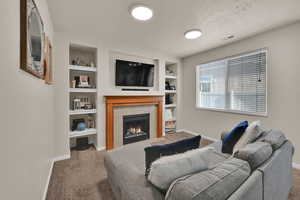 Living room with built in shelves, a tiled fireplace, carpet floors, and a textured ceiling