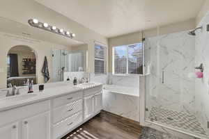 Ensuite bathroom with double vanity, a bath, dark wood-type flooring, and a marble finish shower