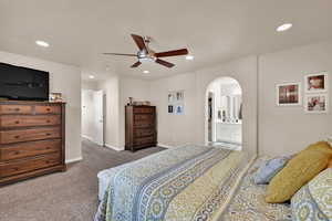 Carpeted bedroom featuring recessed lighting, arched walkways, ceiling fan, and ensuite bathroom