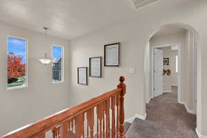 Hallway with an upstairs landing, dark colored carpet, healthy amount of natural light, and arched walkways