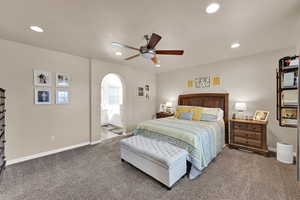 Carpeted bedroom featuring recessed lighting, ceiling fan, arched walkways, and ensuite bath