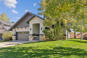 View of front facade featuring stone siding, a front lawn, concrete driveway, stucco siding, and an attached garage