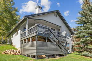 Rear view of house featuring stairway, a lawn, stucco siding, a deck, and a chimney