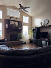 Living room with a ceiling fan, wood finished floors, a fireplace, high vaulted ceiling, and a textured ceiling