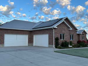 View of property exterior with brick siding, driveway, a garage, and solar panels