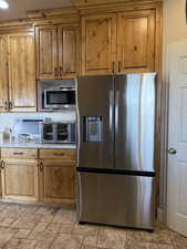Kitchen featuring appliances with stainless steel finishes, brown cabinets, and stone tile floors