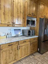 Kitchen featuring appliances with stainless steel finishes, brown cabinets, light stone counters, and light stone finish floors