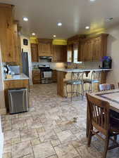 Kitchen with gas stove, a breakfast bar area, recessed lighting, brown cabinetry, and a peninsula
