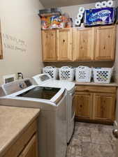 Laundry area with light stone finish floors, cabinet space, and washing machine and dryer