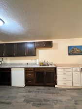 Kitchen featuring a textured ceiling, dark brown cabinetry, white dishwasher, and wood finish floors