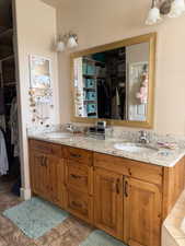 Bathroom with a walk in closet, double vanity, and light stone finish flooring