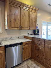 Kitchen with brown cabinetry, dishwasher, light stone counters, and light stone finish floors