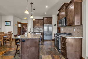 Kitchen featuring dark brown cabinetry, light stone countertops, high quality appliances, hanging light fixtures, and recessed lighting