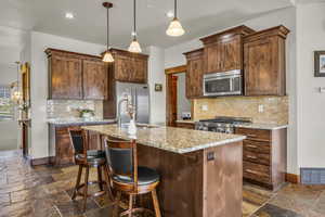 Kitchen featuring decorative light fixtures, backsplash, a center island with sink, light stone countertops, and recessed lighting
