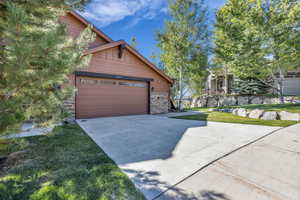 View of front of house featuring stone siding, concrete driveway, board and batten siding, and a front lawn