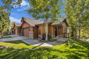 View of front of home with stone siding, a front yard, driveway, and roof with shingles