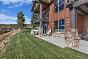 Back of house with board and batten siding, a balcony, a lawn, stone siding, and a patio