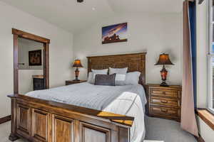 Bedroom featuring light colored carpet, lofted ceiling, and ensuite bathroom