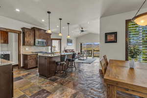 Kitchen with light stone countertops, decorative backsplash, lofted ceiling, a kitchen breakfast bar, and stainless steel appliances