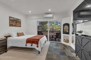 Bedroom with access to exterior, recessed lighting, an AC wall unit, and dark stone finish floors