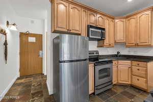 Kitchen featuring stainless steel appliances, dark stone countertops, light brown cabinets, and dark stone finish flooring