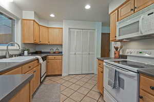 Kitchen with white appliances, dark countertops, light tile patterned floors, recessed lighting, and light brown cabinetry