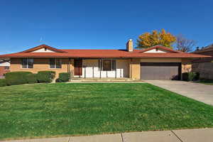Ranch-style house with brick siding, a porch, driveway, a front yard, and a chimney