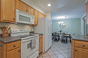 Kitchen featuring dark countertops, white appliances, wallpapered walls, light tile patterned floors, and recessed lighting