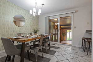 Dining area with wallpapered walls, light tile patterned floors, a textured ceiling, a chandelier, and a wall mounted AC