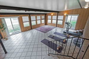 Exercise area with wood walls, light tile patterned floors, and beamed ceiling