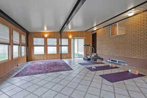 Workout area with wood walls, beamed ceiling, tile patterned floors, and brick wall