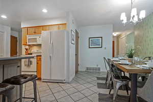 Kitchen featuring white appliances, light tile patterned floors, pendant lighting, a kitchen breakfast bar, and a chandelier