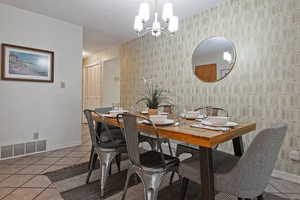 Dining area featuring light tile patterned flooring, a chandelier, and wallpapered walls