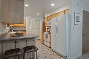 Kitchen with white appliances, light tile patterned floors, recessed lighting, a peninsula, and light brown cabinetry